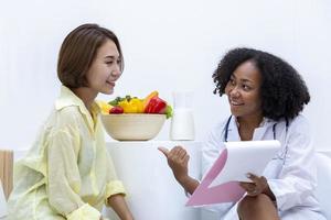 African American nutritionist with bowl of variety of fruit and vegetable giving advice to the client for healthy diet and vitamin booster concept photo