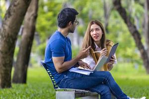 jóvenes estudiantes asiáticos e indios disfrutan de relajarse en el campus universitario mientras se sientan y estudian juntos en el banco durante el fin de semana foto