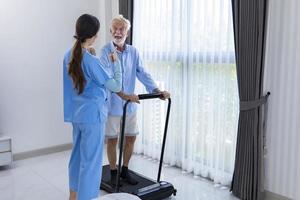 Hospice nurse is supporting Caucasian man to walk using treadmill in pension retirement center for home care rehabilitation and post treatment recovery process photo