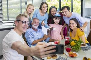 Father taking selfie photo using mobile phone for group photo in his daughter birthday party with whole big family and neighbor joining together in celebration meal