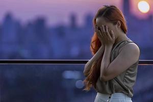 Brunette woman is crying at the balcony during sunset with cityscape view for ptsd and depression from breaking up photo