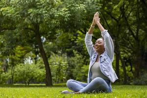 mujer afroamericana relajadamente practicando yoga de meditación y estirándose en el bosque para alcanzar la felicidad de la sabiduría de la paz interior para un concepto sano de la mente y el alma foto