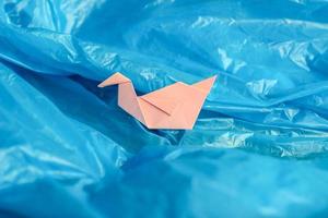 origami de pájaro de papel rosa entre una bolsa de plástico azul como si estuviera en olas de agua o cielo azul. foto conceptual