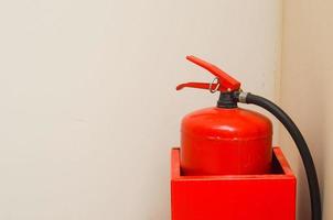 extintor rojo en un recipiente metálico en la esquina de una pared blanca.seguridad. foto