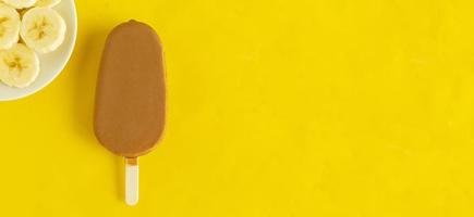 Banana vanilla popsicle in chocolated glaze on bright yellow background. photo