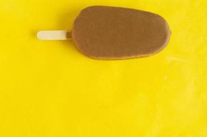 paleta de plátano y vainilla en glaseado de chocolate sobre fondo amarillo brillante, espacio de copia. foto