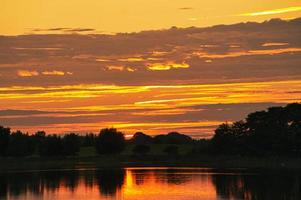 reflejo del cielo en el agua. los colores dorado, amarillo y rosa del cielo se reflejan en el lago. foto