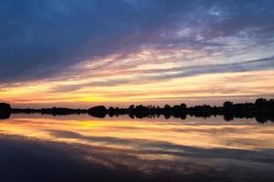 reflejo del cielo en el agua. los colores dorado, amarillo y rosa del cielo se reflejan en el lago. foto