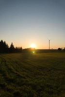 Wind turbine on a hill in front of a field and at the edge of the forest at sunset photo