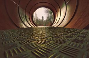 View through a metal pipe. In the background between trees is a water tower. photo