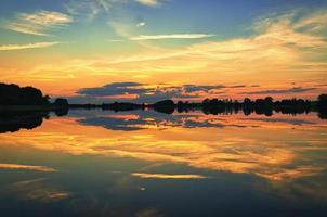 reflejo del cielo en el agua. los colores dorado, amarillo y rosa del cielo se reflejan en el lago. foto