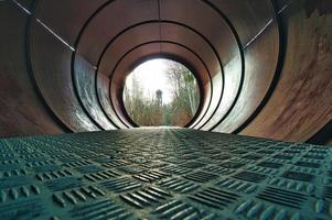 View through a metal pipe. In the background between trees is a water tower. photo