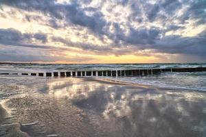 puesta de sol en la playa del mar báltico. reflejo en la playa. los espigones llegan al mar. foto