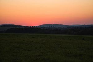 puesta de sol romántica detrás de una colina frente a un prado. foto