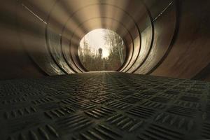 View through a metal pipe. In the background between trees is a water tower. photo