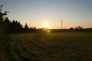 Wind turbine on a hill in front of a field and at the edge of the forest at sunset photo
