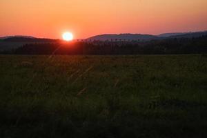 romantic sunset behind a hill in front of a meadow. photo