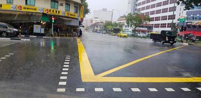 Singapore - June 28, 2021 Road crossing with heavy rain and yellow line on street with building and car background. Traffic on raining day and weather concept. photo