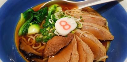 Close up hot ramen noodle with vegetable, sliced spring onion and pot-stewed duck in soup on blue bowl. Famous Japanese food in Asia. photo