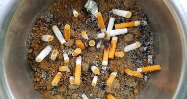 Top view Many cigarette butts in ashtray or sand after people smoked. garbage, pollution or health concept photo