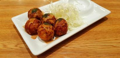 Takoyaki topped with sweet sauce and sliced cabbage in white dish on brown wooden background. Japanese food in plate on wood table with copy space. photo