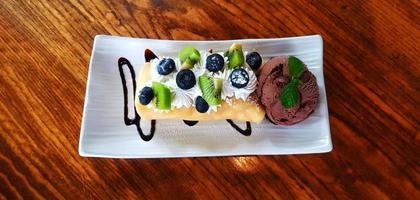 Top view of Chocolate ice cream with sliced fresh kiwi, berry or raspberry and whipped cream in plate or dish on wooden table with copy space at caf. Flat lay of Dessert food with freshness fruit. photo