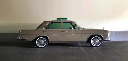 Bangkok, Thailand - June 20, 2022 Brown Mercedes Benz parked in parking with white concrete wall background. Vintage or retro car on street. Classic vehicle on road produces from England and luxury. photo