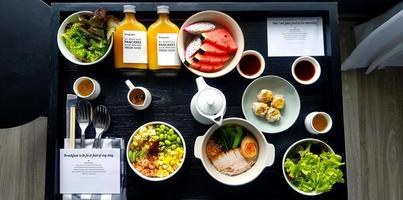Top view of breakfast with fresh salad, dim sum, noodle with boiled pork, watermelon, dragon fruit, bottle of orange juice and sweet sauce. Flat lay of healthy food with vegetable and fruit on table. photo