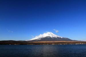 Fuji mountain with snow and fog covered top, lake or sea and clear blue sky background with copy space. This place famous in Japan and Asia for people travel to visit and take picture. photo