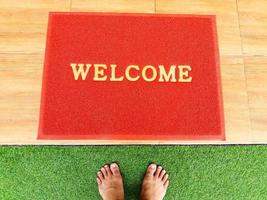 Top view of foots on green grass with red welcome doormat and copy space. photo