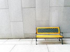 Yellow bench on white or gray concrete wall background with copy space - available seat, alone and relaxing photo