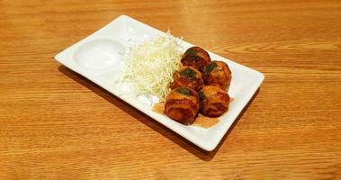 Takoyaki topped with sweet sauce and sliced cabbage in white dish on brown wooden background. Japanese food in plate on wood table with copy space. photo