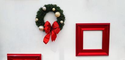 Navidad, decoración de corona de feliz año nuevo con cinta roja, bola blanca y marco rojo para agregar texto aislado en el fondo de la pared blanca. objeto para fiesta decorada, festival con espacio de copia. foto