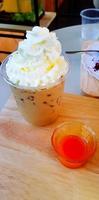 Plastic glass of iced coffee on topped with whipped cream and orange juice on wooden table at cafe. Espresso, cappuccino or mocha and refreshment drinking concept photo