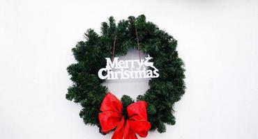 Merry Christmas wreath with green leaves and red ribbon isolated on white background with copy space. Object decorated for party, festival or event on concrete wall or wallpaper. photo