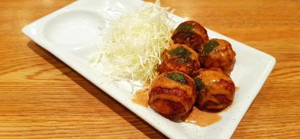 takoyaki cubierto con salsa dulce y repollo en rodajas en un plato blanco sobre fondo de madera marrón. comida japonesa en plato sobre mesa de madera con espacio para copiar. foto