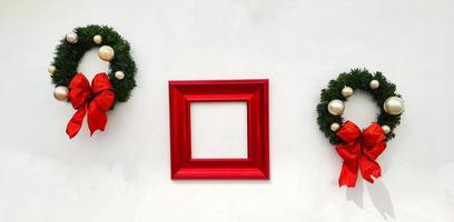 Navidad, decoración de corona de feliz año nuevo con cinta roja, bola blanca y marco rojo para agregar texto aislado en el fondo de la pared blanca. objeto para fiesta decorada, festival con espacio de copia. foto