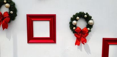 Navidad, decoración de corona de feliz año nuevo con cinta roja, bola blanca y marco rojo para agregar texto aislado en el fondo de la pared blanca. objeto para fiesta decorada, festival con espacio de copia. foto