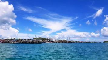 Many fishing boat parked on sea at port near coast and community with blue sky, white clouds and green mountain background and copy space. Landscape of ocean or seascape. Beautiful view and nature photo