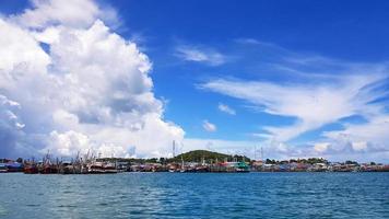 muchos barcos de pesca estacionados en el mar en el puerto cerca de la costa y la comunidad con cielo azul, nubes blancas y fondo de montaña verde y espacio para copiar. paisaje de océano o paisaje marino. hermosa vista y naturaleza foto