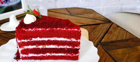 Piece of red velvet cake in white dish on wooden table at cafe. Sweet food or dessert on plate. photo