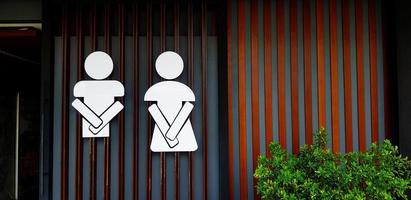 Public toilet sign or symbol of man and woman on wooden and gray or grey wall background with copy space. Entrance of restroom or lavatory with tree in front of room. photo