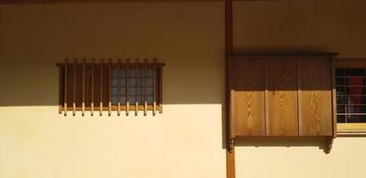 Brown wooden and dry bamboo window with shadow on yellow concrete wall background in. Exterior design by use natural material to build house or home at Japan. Object decorated and art of light. photo