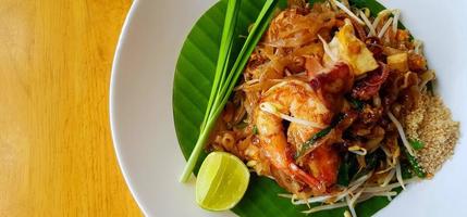 Top view of stir fried with rice noodle, river prawn or shrimp, bean sprout, sliced chives and lime on banana leaf with copy space. Famous food in Thailand call Pad Thai. Selective focus technique. photo