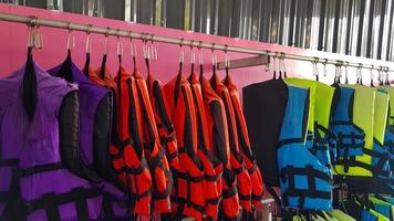 Many purple or violet, red, blue and green life jacket hanging on stainless steel hanger for people or group of tourist rent and wear for safety when take a boat or speed boat on sea or ocean. photo