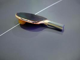 High angle view of dilapidated  table tennis bat and ball on dark color table photo