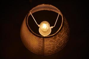 Incandescent lamp in round lampshade glowing in dark. photo