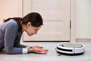 Friendly cheerful woman looking at robotic vacuum cleaner. photo
