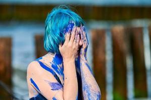 Artistic blue-haired woman performance artist in dress smeared with blue gouache paints on her body photo