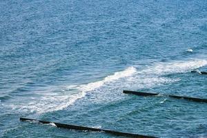 Vintage long wooden breakwaters stretching far out to deep blue sea waters, foaming waves, seascape photo